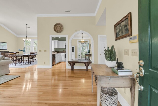 foyer featuring light wood finished floors, a chandelier, arched walkways, crown molding, and baseboards