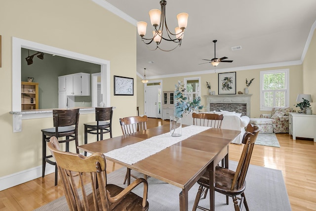 dining area with light wood-type flooring, ornamental molding, a ceiling fan, baseboards, and a fireplace