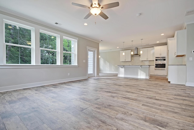 unfurnished living room featuring ceiling fan, ornamental molding, and light wood-type flooring