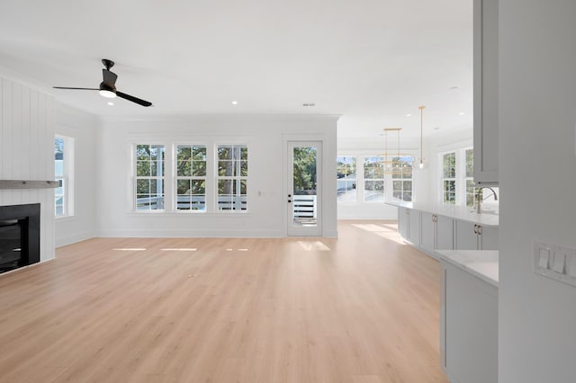 unfurnished living room featuring crown molding, a fireplace, light hardwood / wood-style floors, and ceiling fan