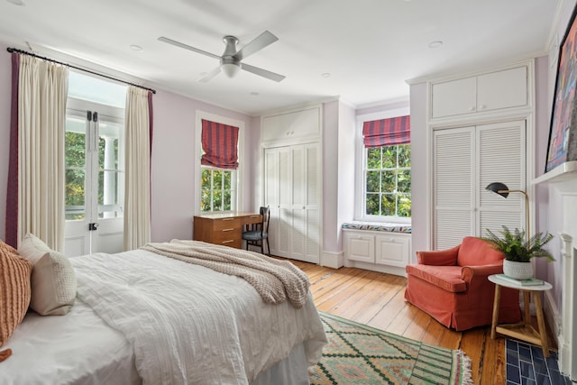 bedroom featuring ceiling fan, ornamental molding, light hardwood / wood-style floors, and multiple closets