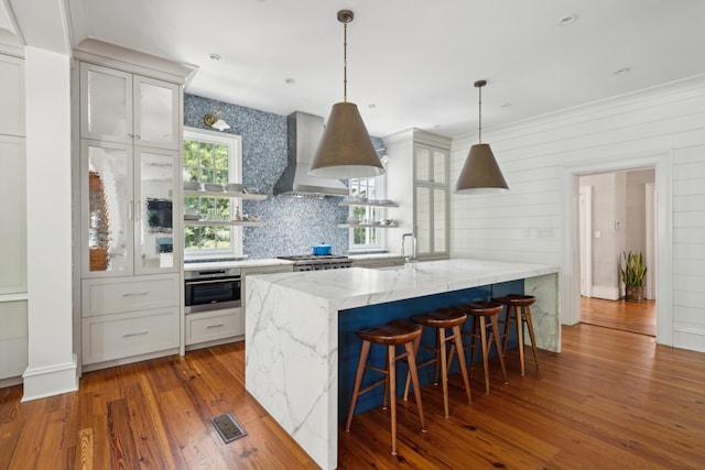 kitchen with white cabinetry, hanging light fixtures, stainless steel appliances, light stone counters, and wall chimney exhaust hood