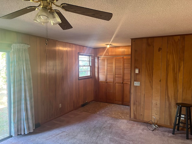 empty room featuring carpet flooring, a textured ceiling, ceiling fan, and wood walls