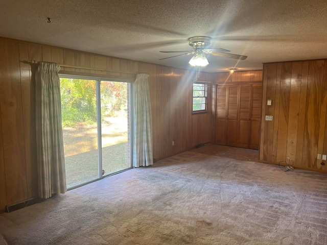 unfurnished room featuring a textured ceiling, light colored carpet, ceiling fan, and wooden walls