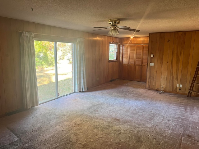 carpeted spare room with ceiling fan, wood walls, and a textured ceiling