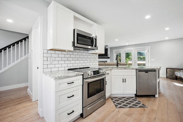 kitchen featuring decorative backsplash, light wood-style flooring, appliances with stainless steel finishes, a peninsula, and a sink