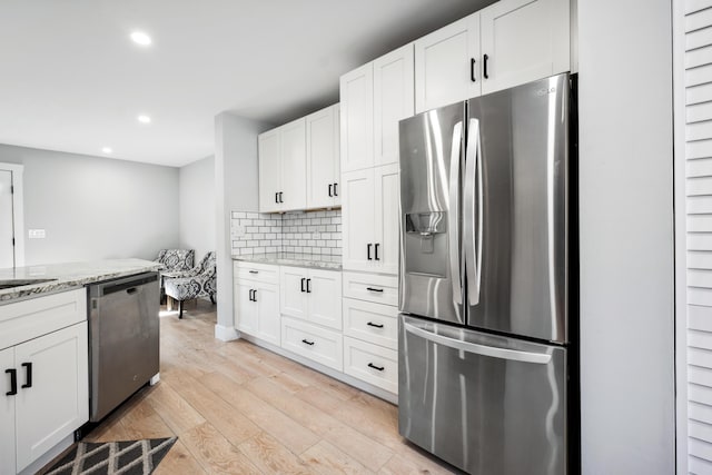 kitchen featuring light wood-style flooring, white cabinets, appliances with stainless steel finishes, light stone countertops, and tasteful backsplash