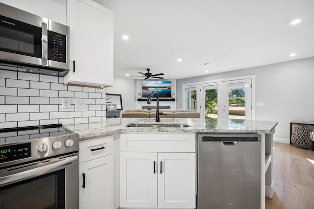 kitchen with light stone counters, appliances with stainless steel finishes, white cabinetry, a sink, and a peninsula