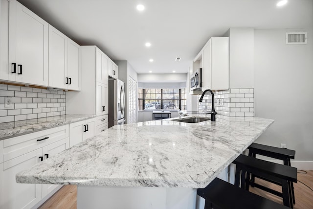 kitchen with light stone counters, stainless steel appliances, a breakfast bar, a sink, and white cabinets