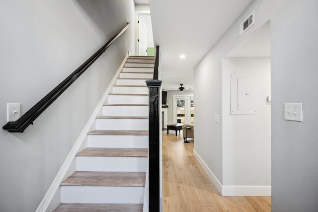 stairs featuring visible vents, a ceiling fan, baseboards, electric panel, and wood-type flooring