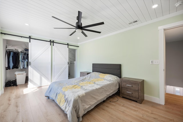 bedroom with a barn door, visible vents, baseboards, light wood-style flooring, and ornamental molding