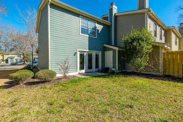 rear view of property with a lawn, a chimney, and fence