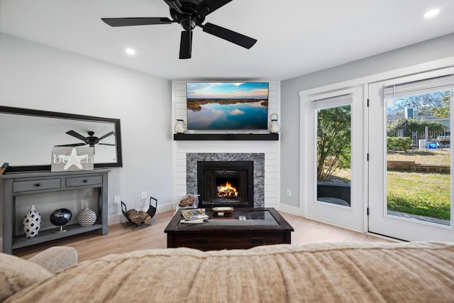 living room with recessed lighting, a warm lit fireplace, baseboards, and wood finished floors