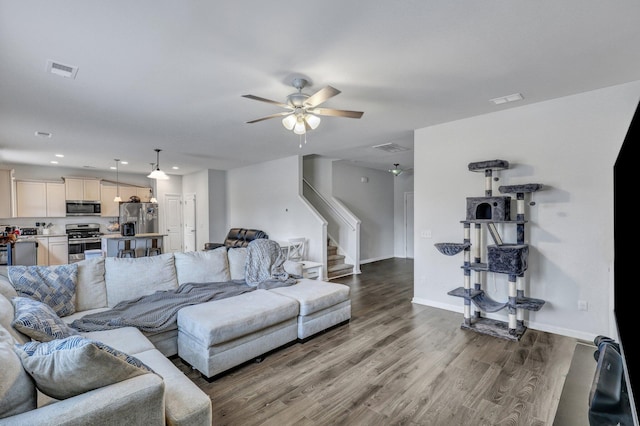 living room with visible vents, ceiling fan, baseboards, stairway, and wood finished floors