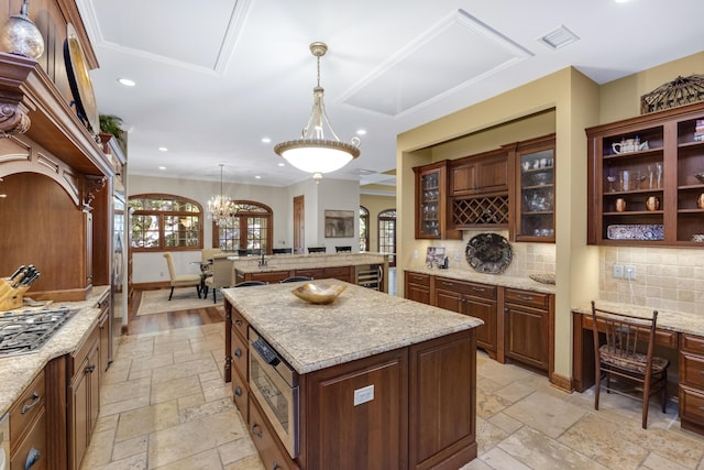 kitchen with hanging light fixtures, a kitchen island, glass insert cabinets, and stone tile flooring