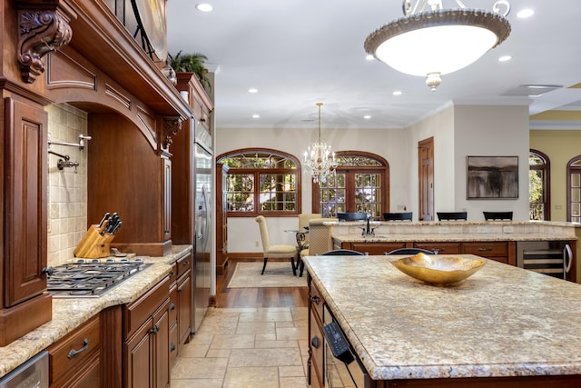 kitchen with a kitchen island with sink, decorative light fixtures, ornamental molding, appliances with stainless steel finishes, and stone tile flooring