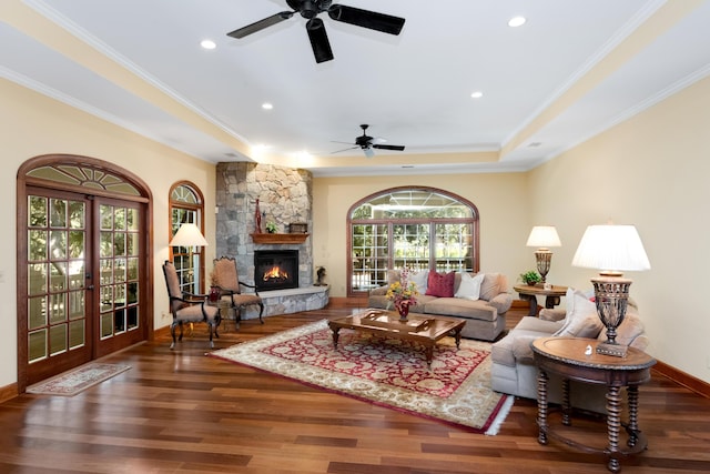 living area featuring baseboards, a stone fireplace, dark wood finished floors, and crown molding