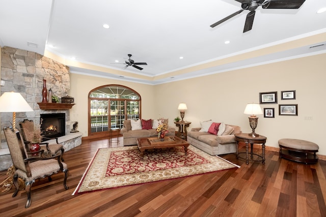 living area with visible vents, a ceiling fan, wood finished floors, crown molding, and a fireplace