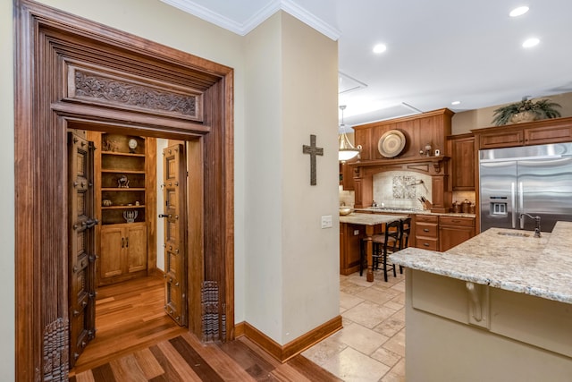 kitchen with stainless steel appliances, a sink, baseboards, ornamental molding, and brown cabinetry