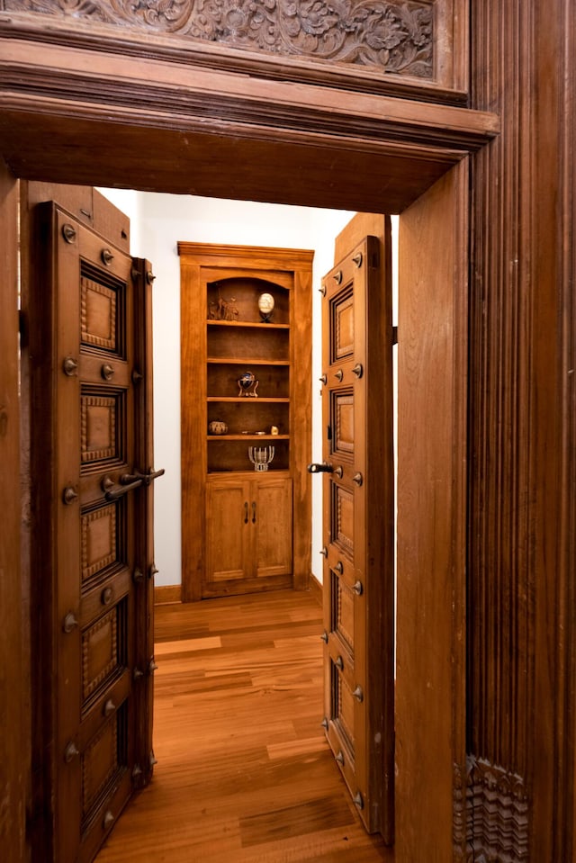 corridor with light wood finished floors and built in shelves