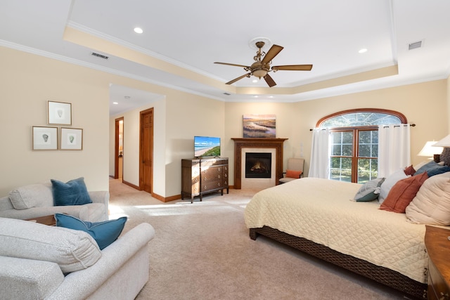 bedroom featuring a tray ceiling, light carpet, a glass covered fireplace, and visible vents