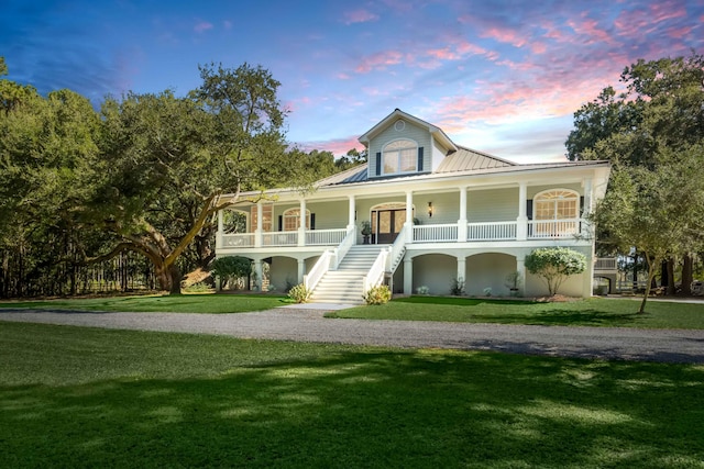 view of front of house featuring a porch, metal roof, a lawn, and stairway