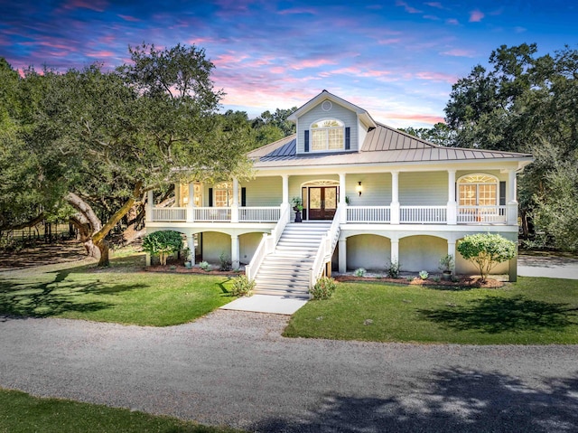 view of front facade featuring driveway, stairway, metal roof, covered porch, and a yard