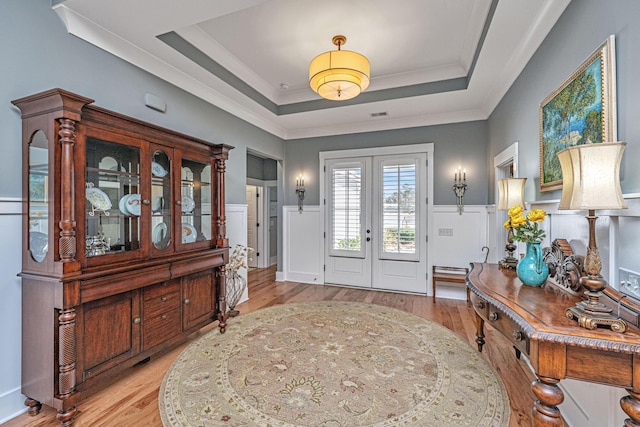 entrance foyer with light wood-style flooring, a wainscoted wall, french doors, a tray ceiling, and crown molding