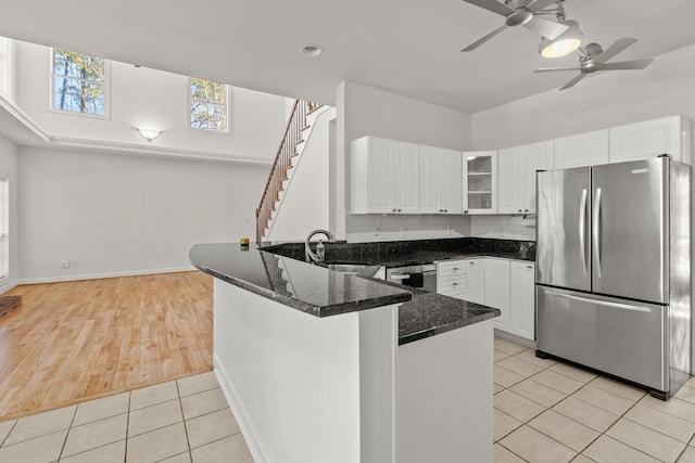 kitchen with dark stone counters, light tile patterned floors, appliances with stainless steel finishes, a peninsula, and a sink