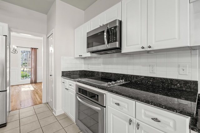 kitchen featuring light tile patterned floors, dark stone counters, decorative backsplash, appliances with stainless steel finishes, and white cabinetry