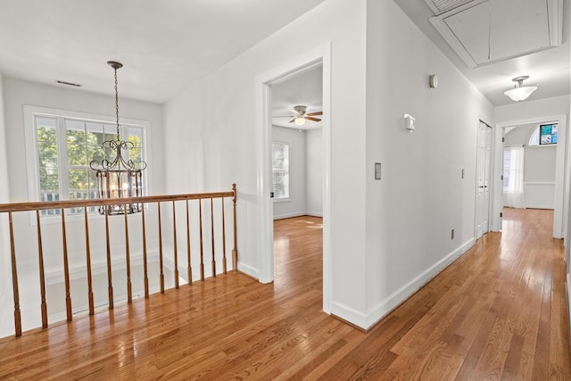 hall featuring visible vents, an upstairs landing, light wood-style flooring, baseboards, and attic access