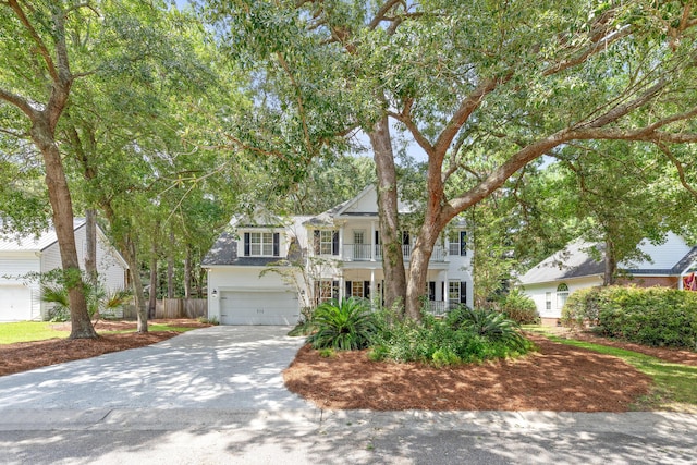 colonial inspired home featuring concrete driveway, covered porch, fence, a balcony, and a garage