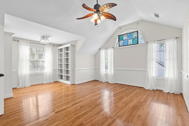 additional living space featuring a ceiling fan, visible vents, light wood finished floors, vaulted ceiling, and wainscoting