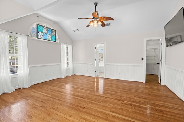 unfurnished living room with visible vents, a ceiling fan, and a wainscoted wall