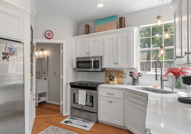 kitchen featuring light wood finished floors, stainless steel appliances, white cabinetry, pendant lighting, and a sink