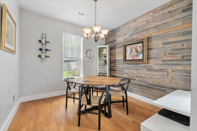 dining area featuring wood walls, light hardwood / wood-style floors, and an inviting chandelier