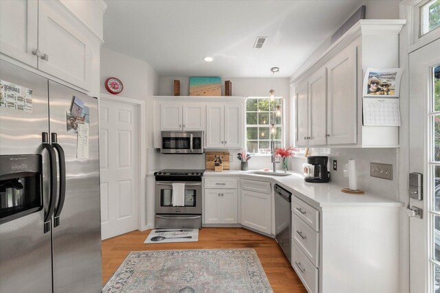 kitchen featuring stainless steel appliances, light hardwood / wood-style floors, white cabinetry, sink, and pendant lighting