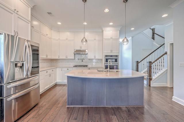 kitchen featuring stainless steel appliances, dark hardwood / wood-style floors, pendant lighting, white cabinets, and a center island with sink