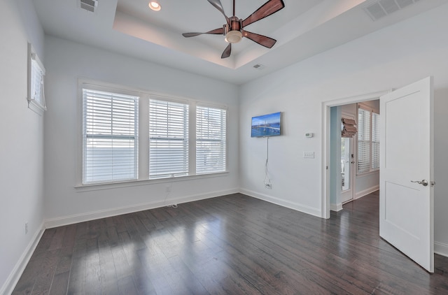 empty room with ceiling fan, a tray ceiling, and dark hardwood / wood-style flooring