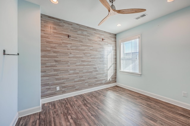 empty room featuring ceiling fan, hardwood / wood-style flooring, and tile walls