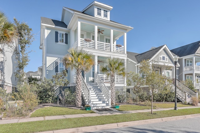 raised beach house featuring a balcony, a front yard, and ceiling fan