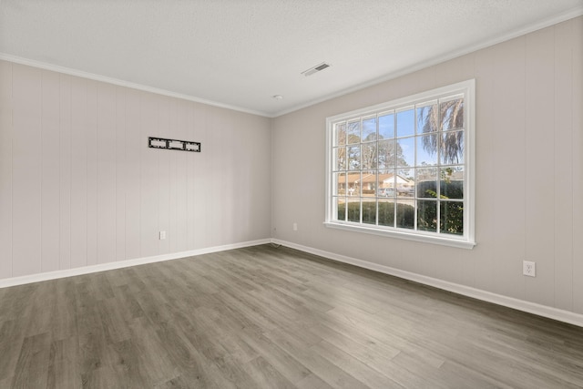 empty room with hardwood / wood-style flooring, wood walls, ornamental molding, and a textured ceiling