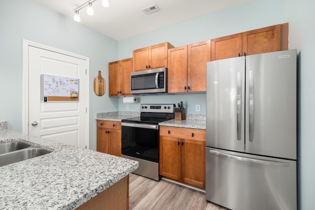 kitchen featuring light stone countertops, appliances with stainless steel finishes, light wood-type flooring, and track lighting