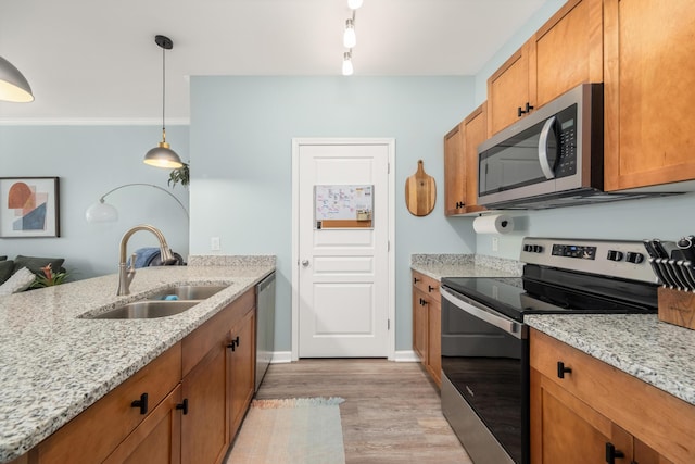 kitchen with hanging light fixtures, sink, light hardwood / wood-style flooring, light stone countertops, and appliances with stainless steel finishes