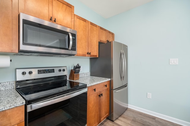 kitchen with light stone countertops, appliances with stainless steel finishes, and wood-type flooring