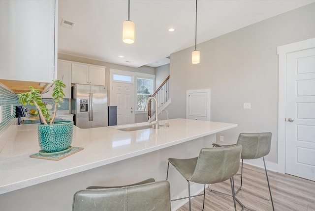 kitchen with visible vents, light wood-style floors, a sink, stainless steel fridge, and a peninsula