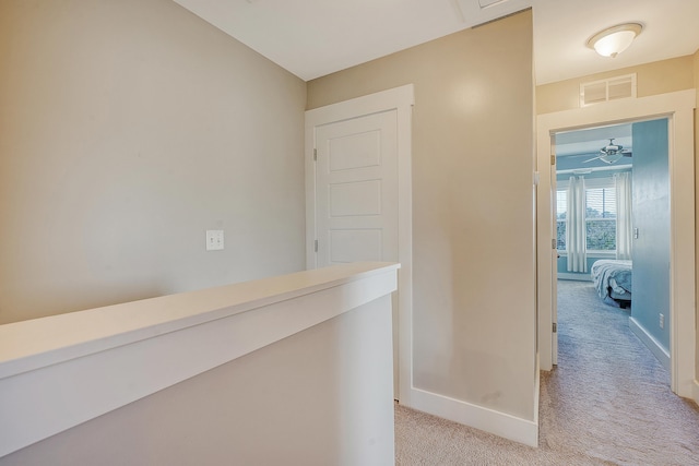 hallway featuring light colored carpet, visible vents, and baseboards