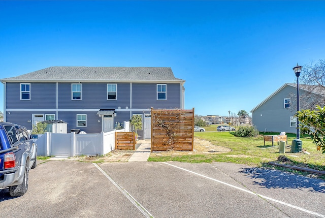 back of house with uncovered parking, fence, and a lawn