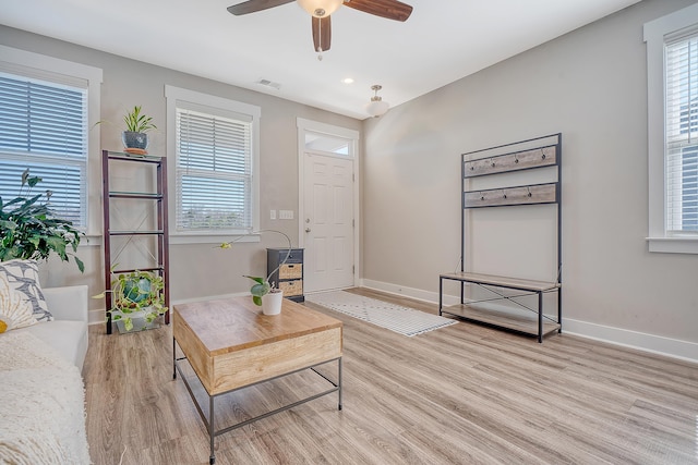 living room with light wood-style floors, baseboards, visible vents, and a ceiling fan