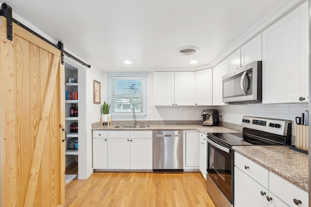 kitchen featuring a barn door, white cabinets, stainless steel appliances, light wood-style floors, and a sink